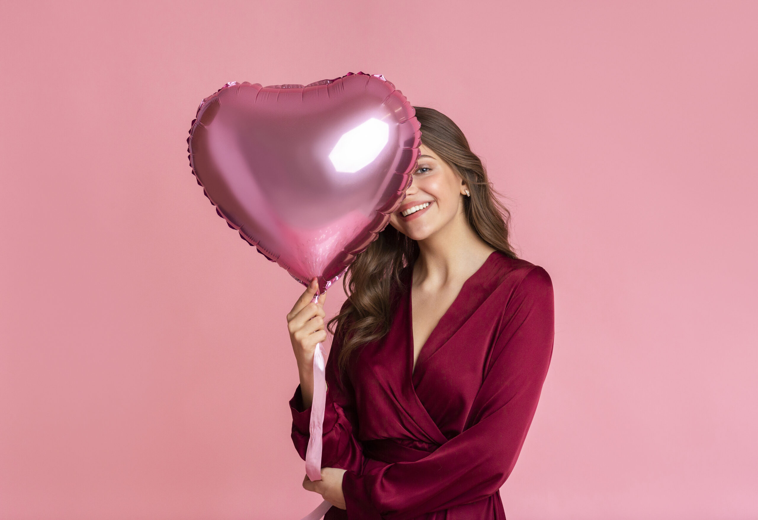 Valentine's Day Offer. Playful Beautiful Girl Covering Her Face With Heart Shaped Balloon, Posing Over Pink Background With Free Space